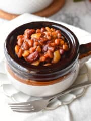 Baked beans in a bean crock with white linens and a fork.