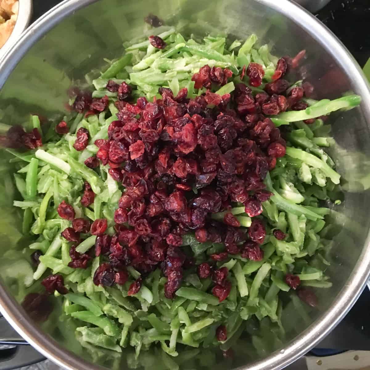 Bright french style green beans are mixed with dried cranberries in a large stainless steel bowl.