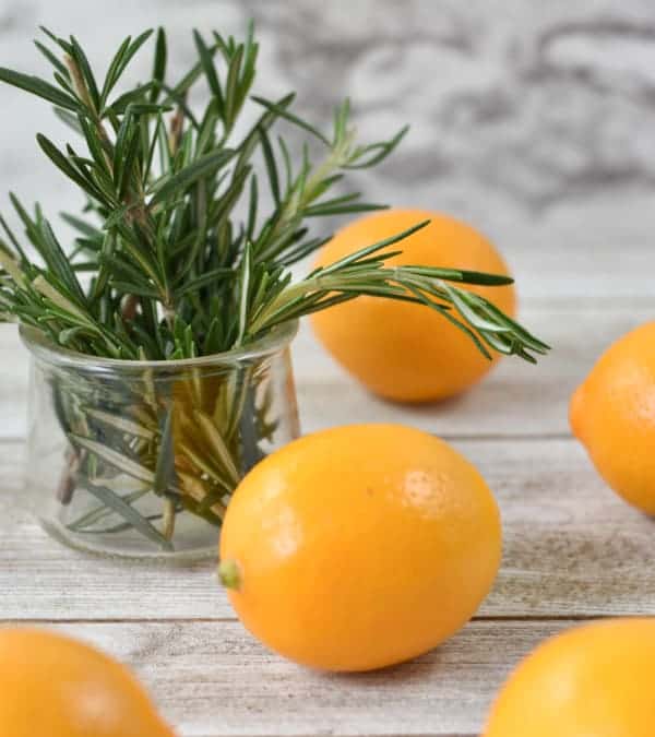 Sprigs of Rosemary in a Glass Container and Meyer Lemons Scattered on a White Washed Rustic Table