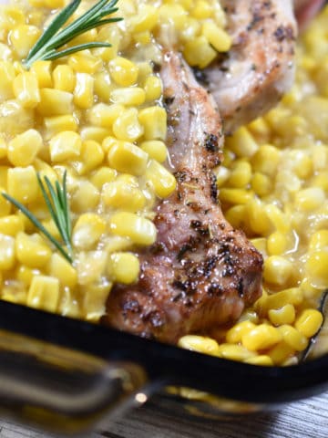 Beautifully browned pork chops are smothered in creamed corn in a smoked glass baking dish.