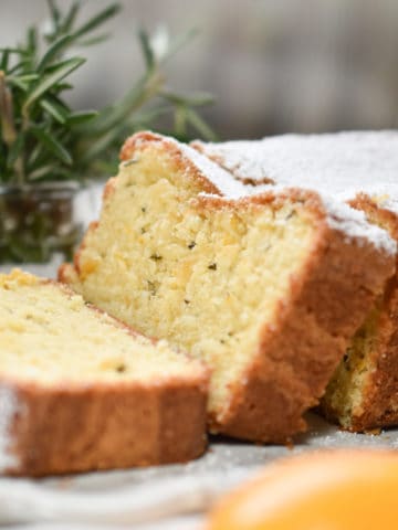 Rich and tender yellow loaf cake with meyer lemon and rosemary flavors is sliced and dusted with powdered sugar.