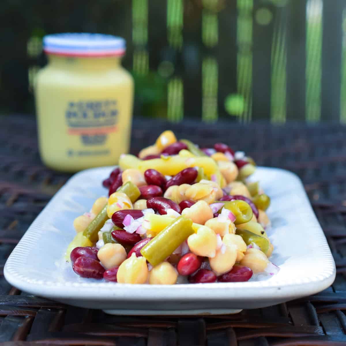 Four bean salad on a white platter with a mustard jar in the background.