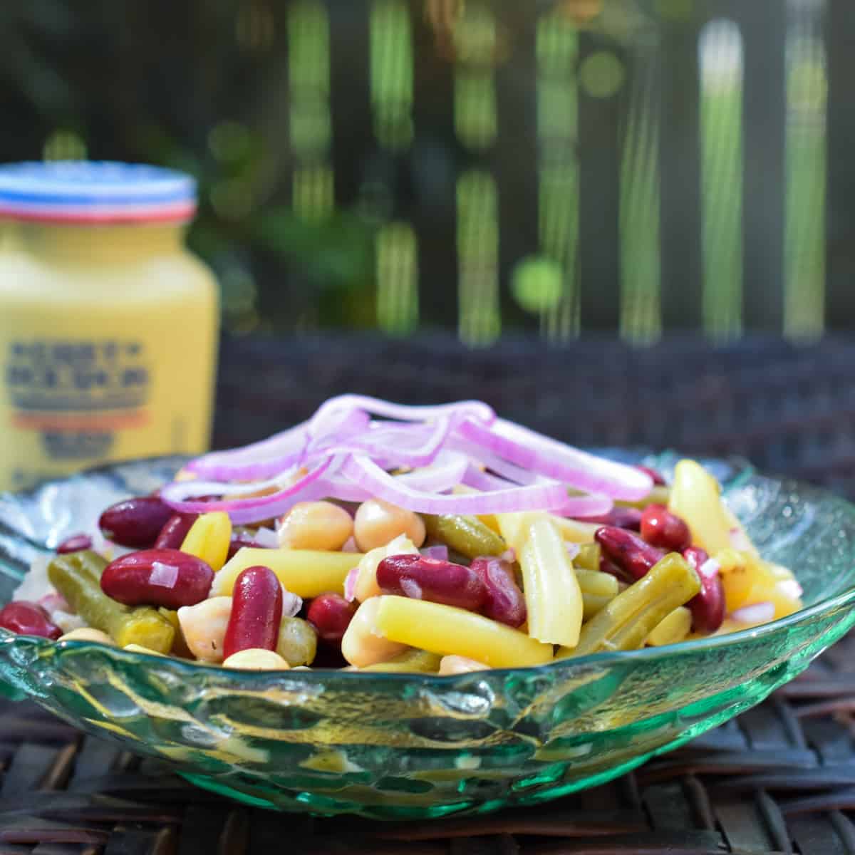 Four bean salad in a green glass bowl and mustard jar in the background.