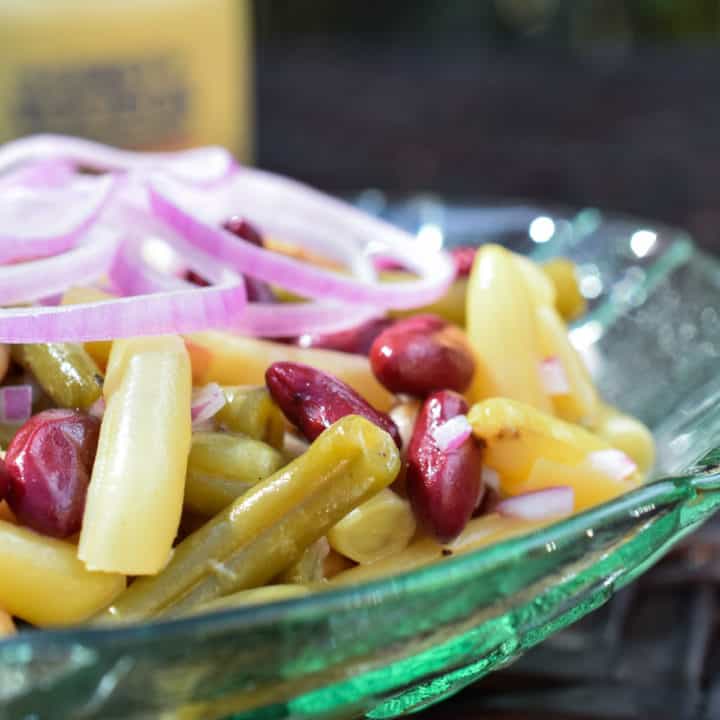 Close up of a four bean salad in a green glass bowl and mustard jar in the background.