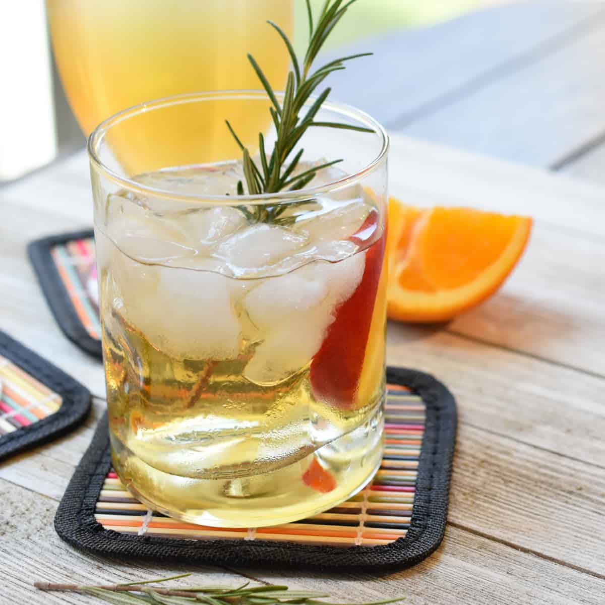 A lillet cocktail in a rocks glass garnished with rosemary and a slice of nectarine.