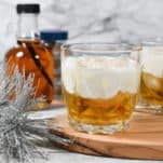 Jim Beam Maple Bourbon and cream cocktail on the rocks with a float of luscious cream. Maple syrup and whole nutmeg are in the backfround.