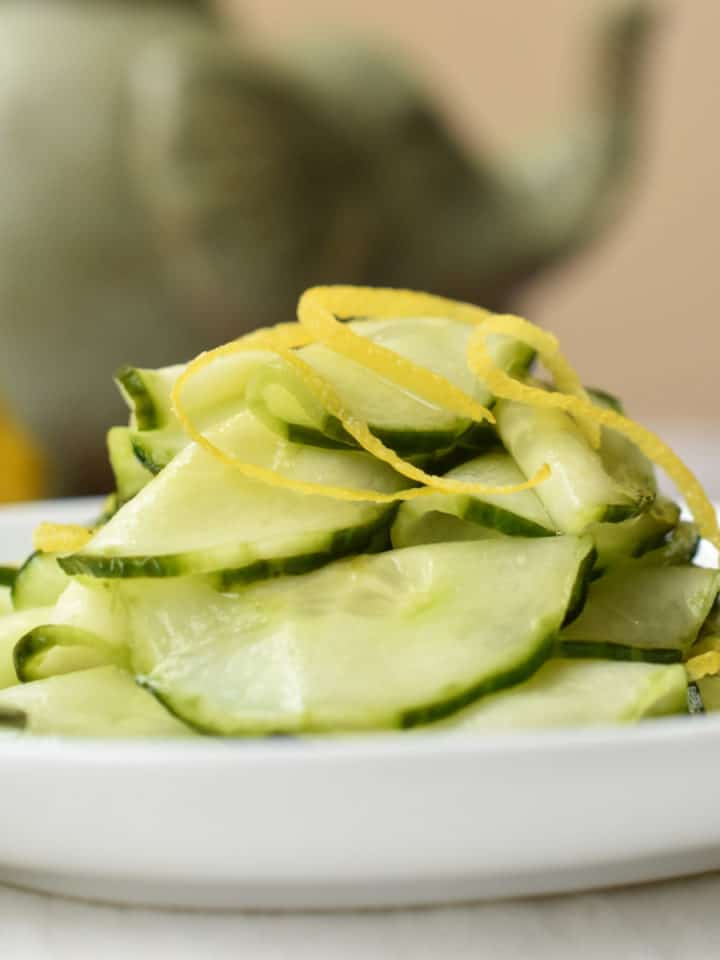 Slices of pickled cucumber are piled on a white dish.