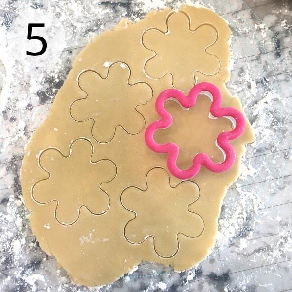Cookie dough is rolled out and cut with a flower cutter.