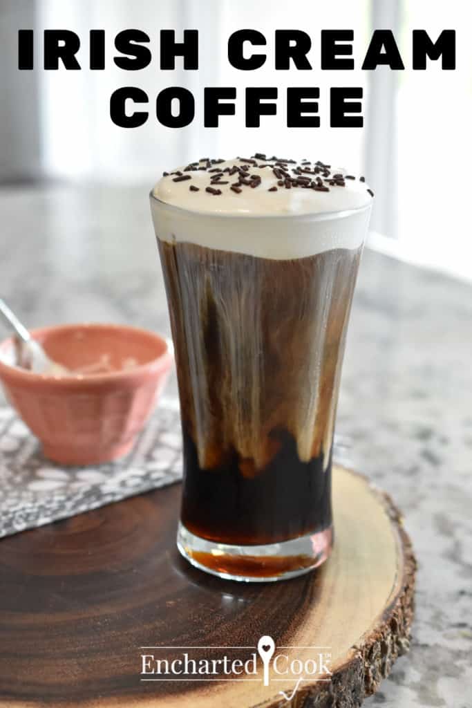 An iced coffee with a rich cream topping and chcoloate sprinkles on a wood tray. A small peach colored bowl with a spoon is in the background.