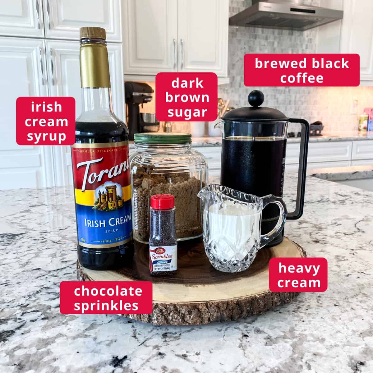 Ingredients on a cut log board, clockwise from top right: Brewed black coffee, heavy cream, chocolate sprinkles, irish cream syrup, dark brown sugar.