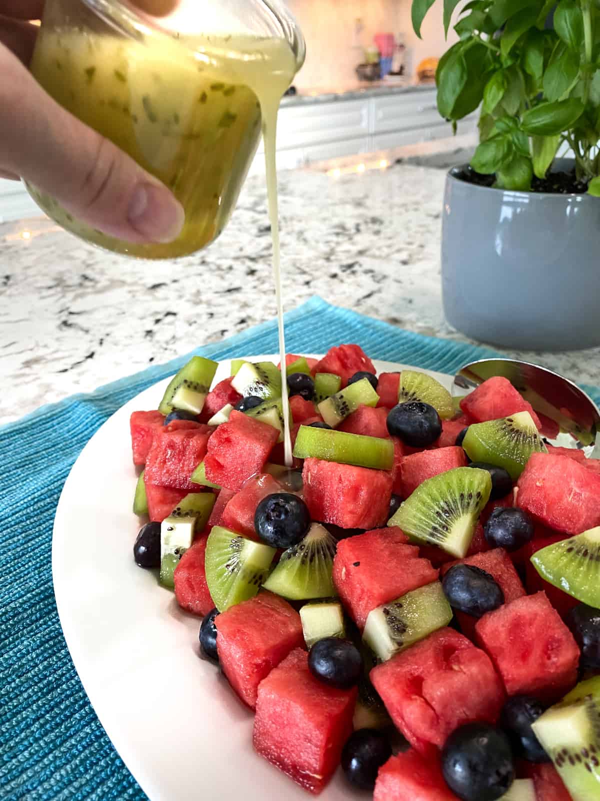 Pale green dressing is being poured over bright red watermelon, kiwis, and blueberries.