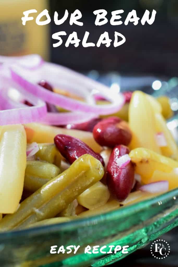 Close up view of bean salad in a clear glass bowl, garnished with rings of red onions. Pinterest Pin #16.