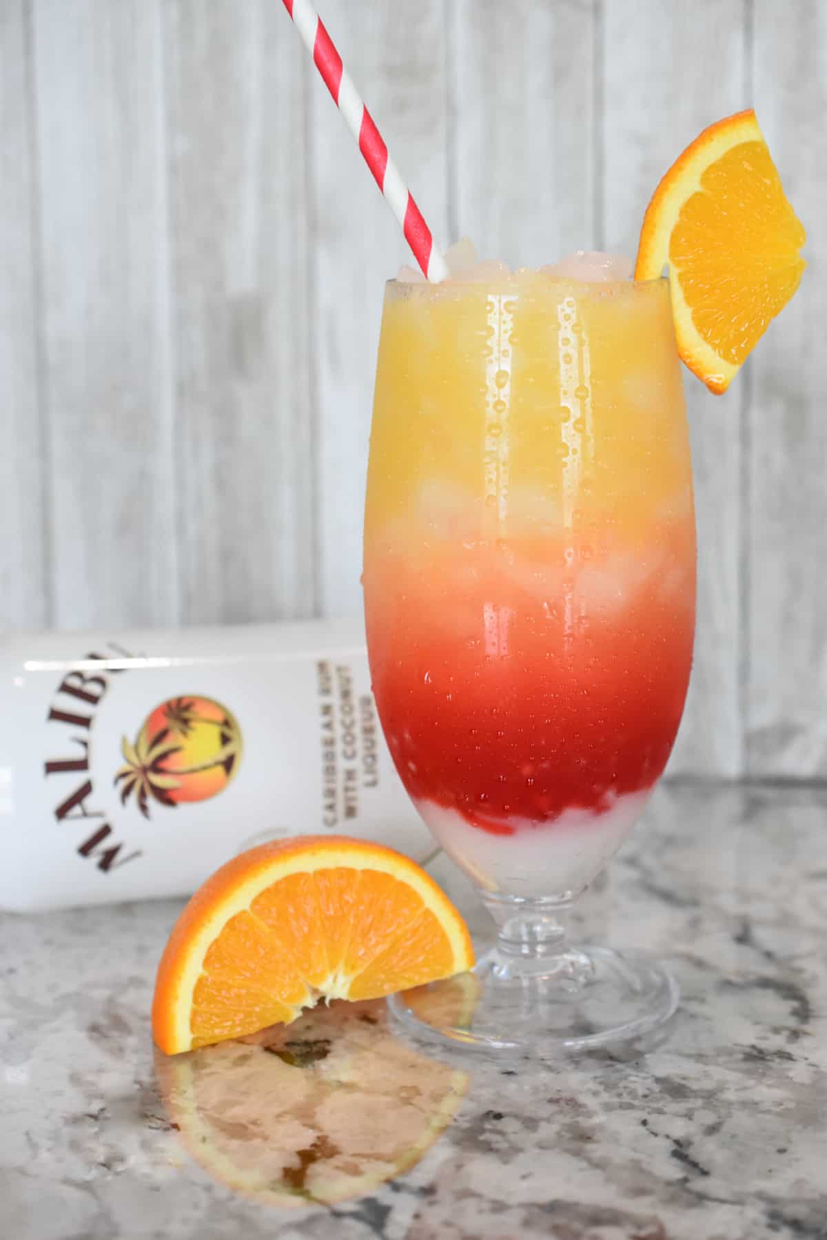 Portrait image of a beautiful layered cocktail of light orange to dark red in a tall glass with crushed ice.