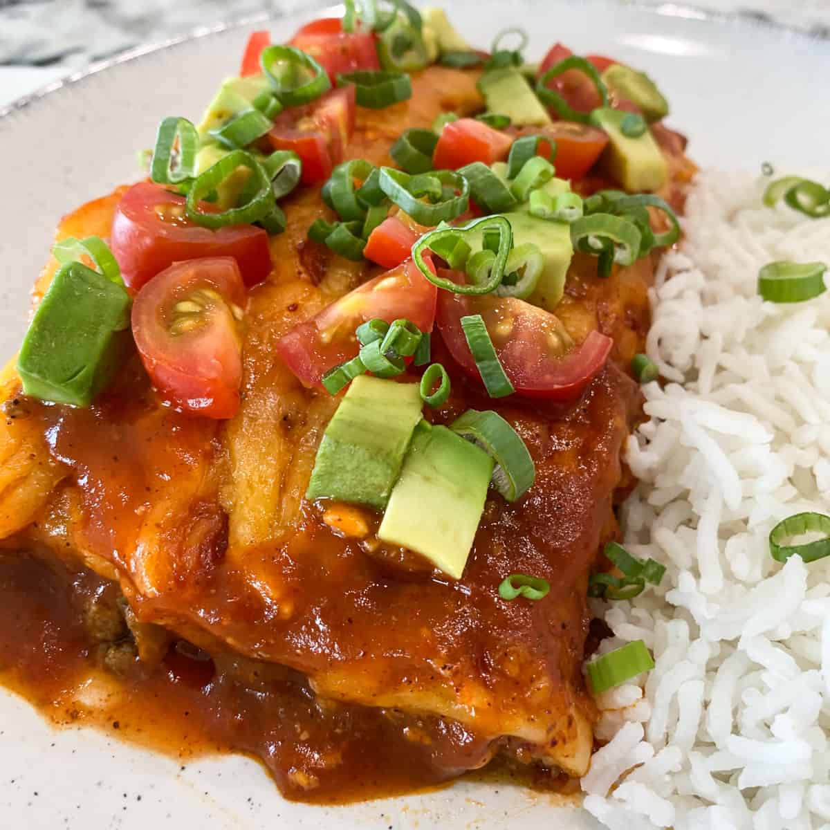 Enchiladas on a plate with white rice and green oinion garnish.