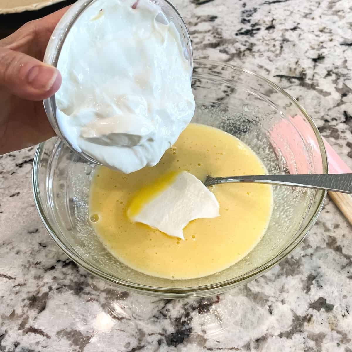 Sour cream is added to the egg mixture in a medium sized glass bowl.