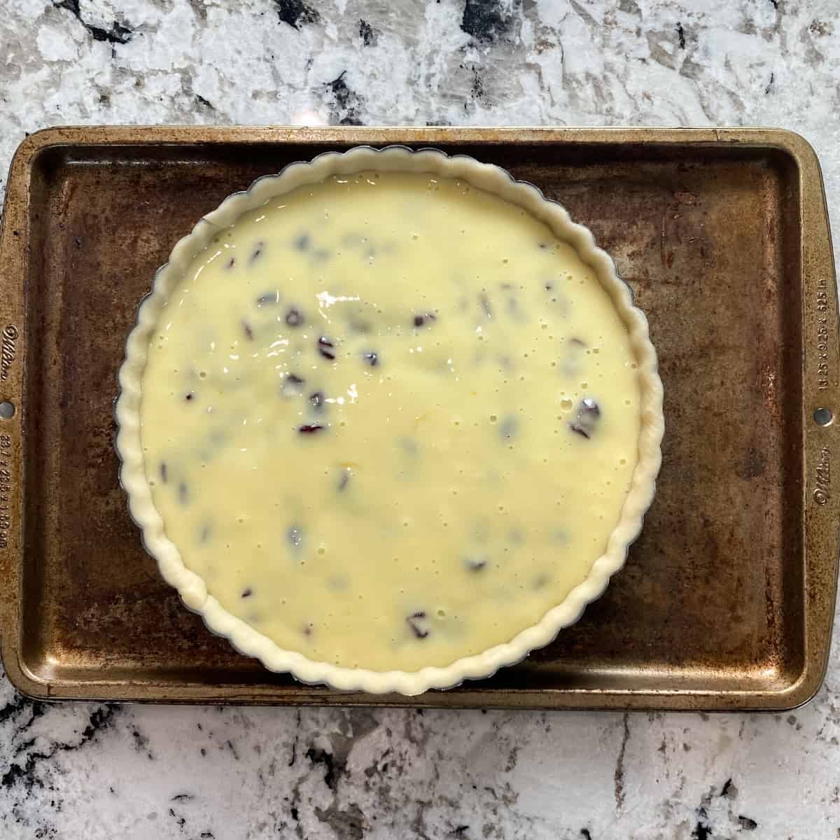 The pie filling has been poured into the prepared tart shell. The tart pan is on a well used baking sheet.