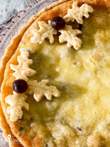 Very close up overhead view of a pie in a tart shell decorated with pie crust leaves and cranberries on a pale pink glass plate.