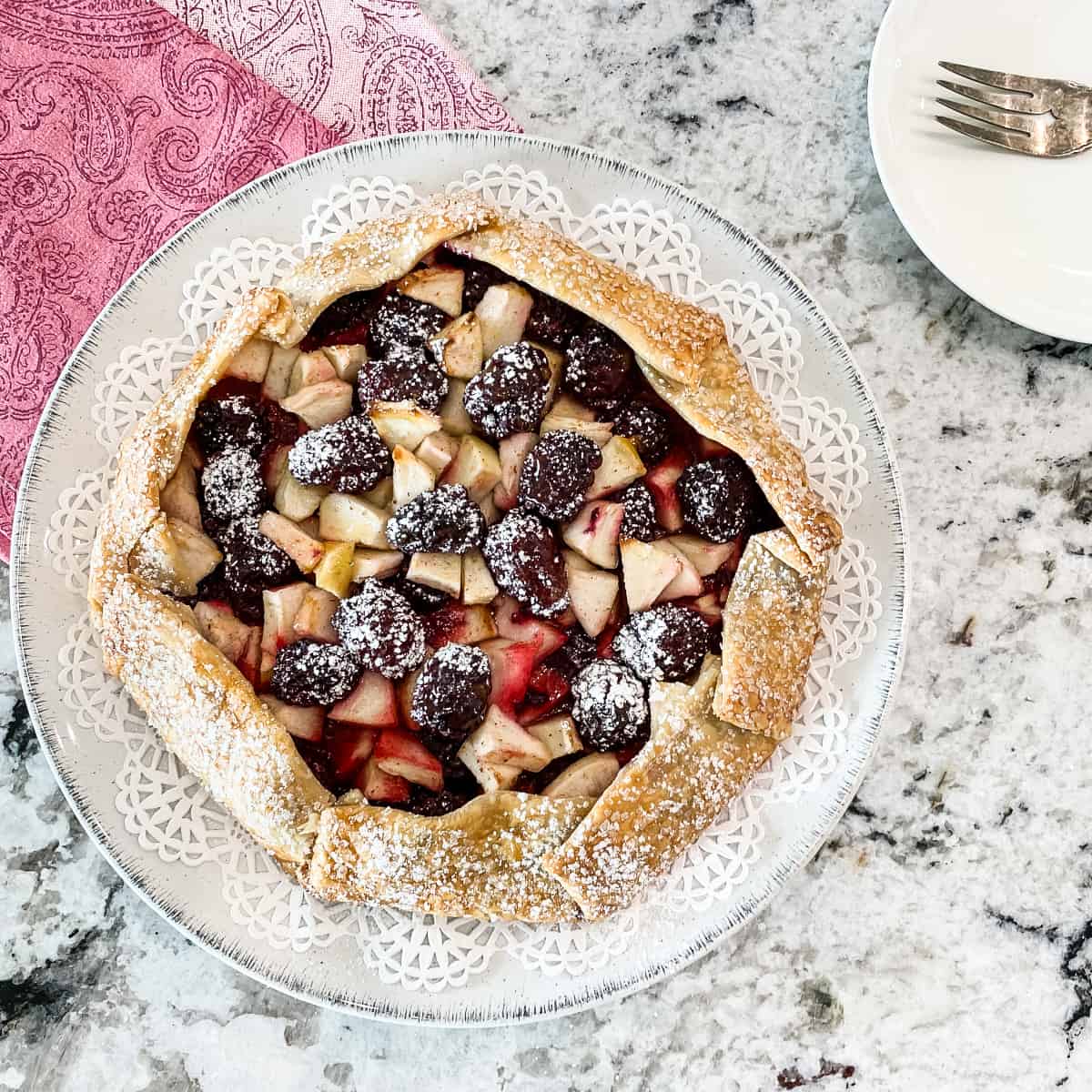 Square image of a rustic tart filled with apple and berries.