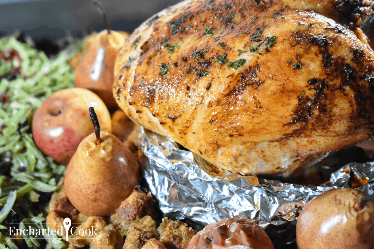 A roasted turkey breast on a homemade aluminum foil rack surrounded by baked apples, pears, dressing, and green beans.