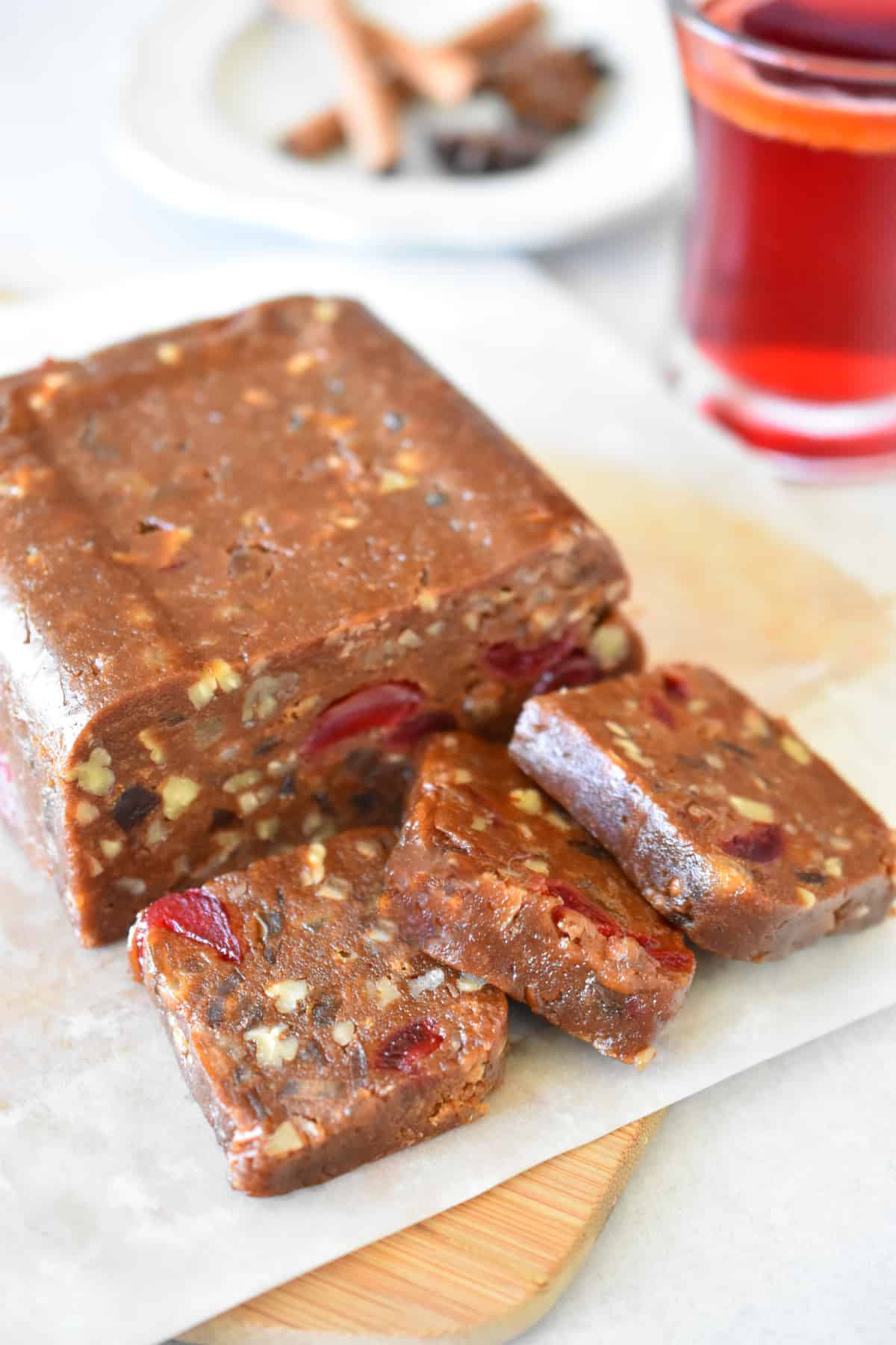 A loaf of fruitcake with a few square slices on a parchment paper covered cutting board.