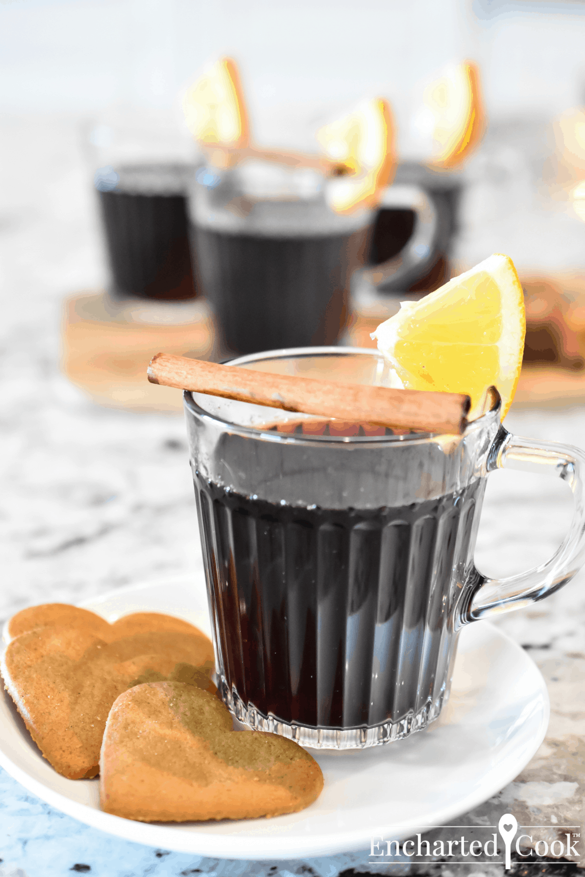 Deep red wine in a clear glass mug garnished with a slice of orange and a cinnamon stick.