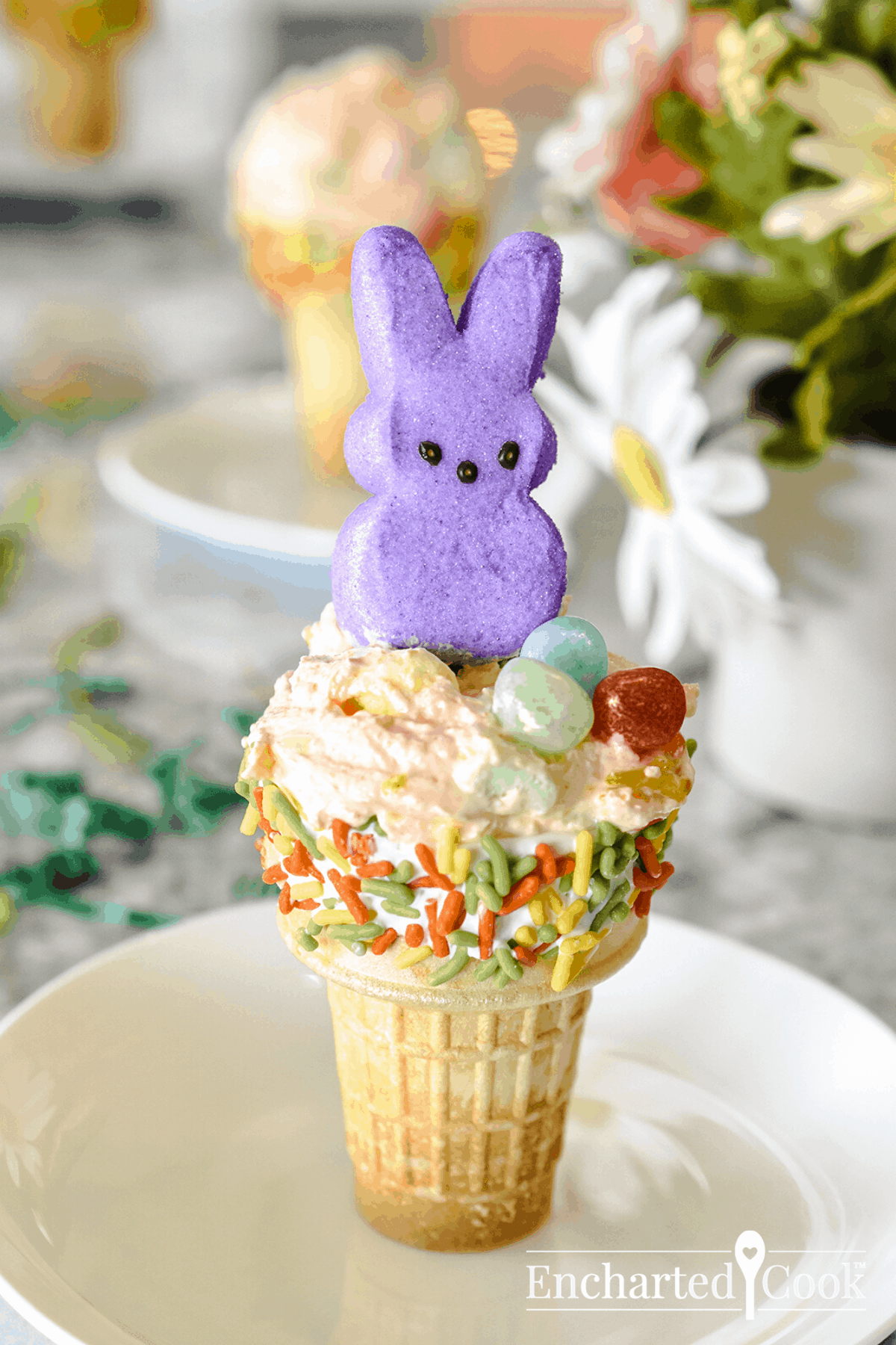 A cake cone is dipped in white candy melts and colorful jimmies and filled with fluff. A peeps bunny and jelly beans decorate the top.