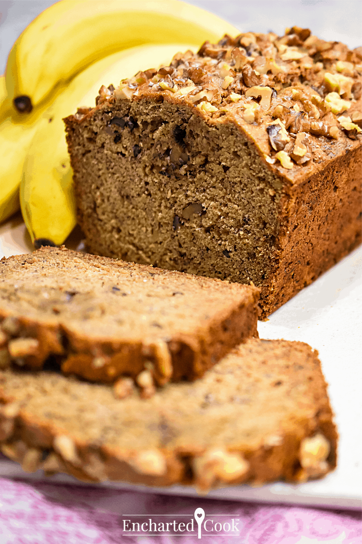 Portrait image of a sliced loaf of banana bread with bananas in the background.