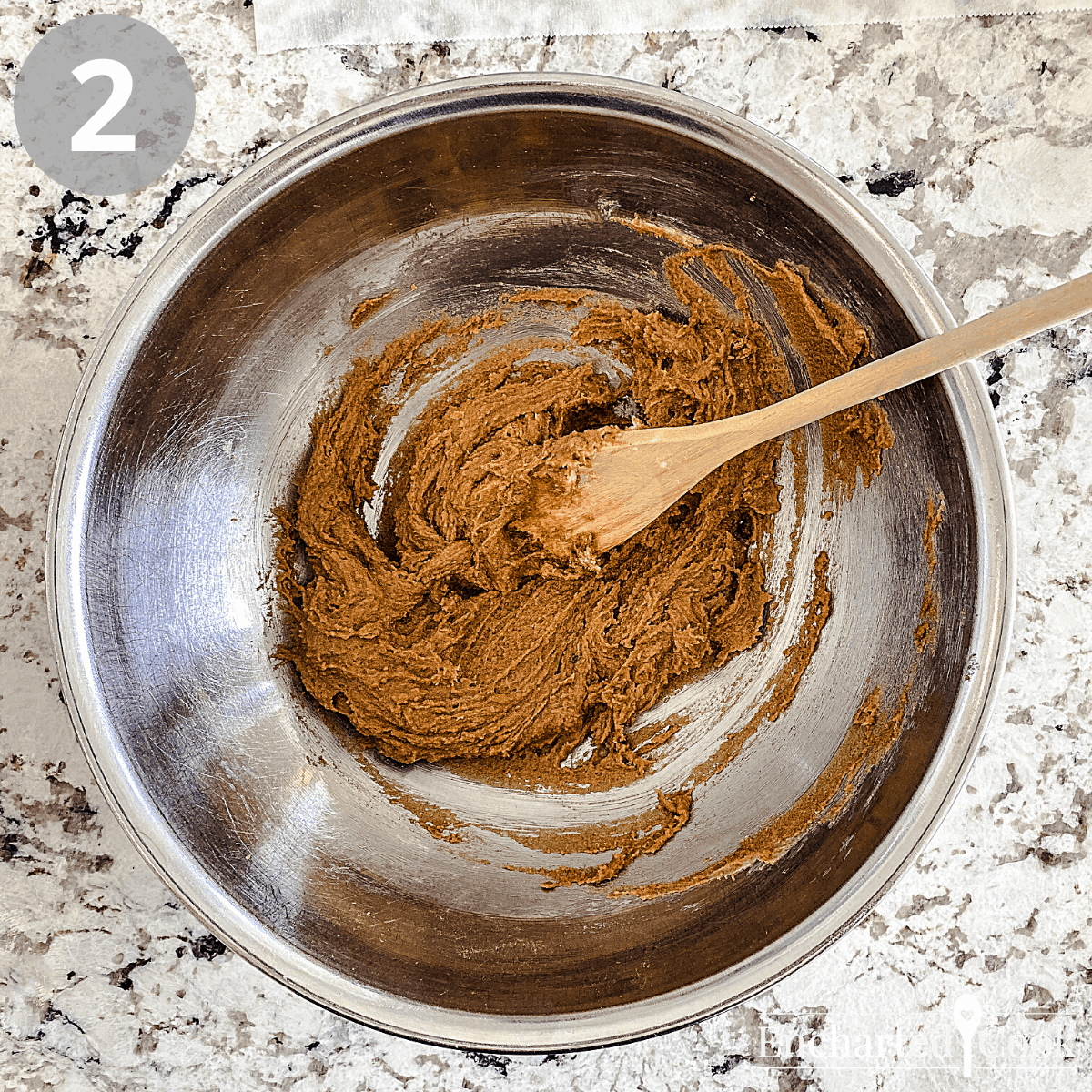 A large bowl contains a beaten mixture of dark brown sugar, butter, and other ingredients.