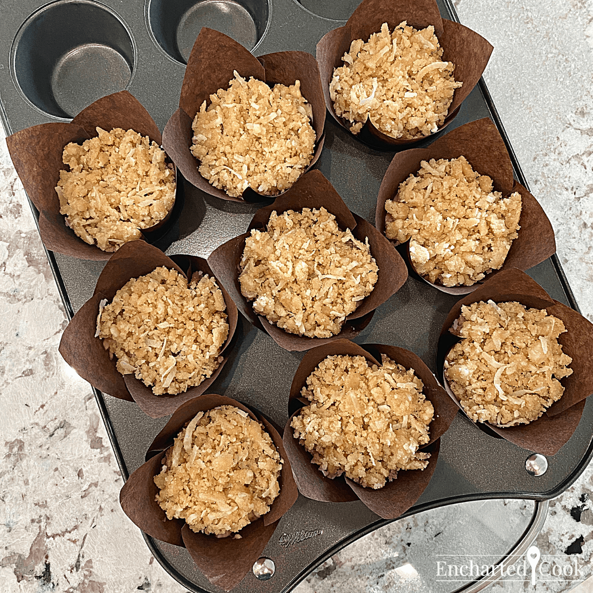 The muffins are ready for the oven. Each muffin cup is filled with the banana chocolate chip batter and each muffin is topped with the coconut crumb topping.