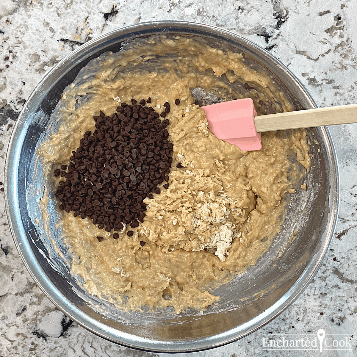 The flour has been folded into the batter and mini chocolate chips are ready to be folded into the batter with a rubber spatula.