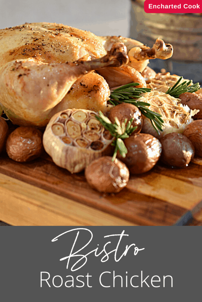 A golden brown roasted chicken is surrounded by roasted red potatoes and garlic on a heavy wooden cutting board.