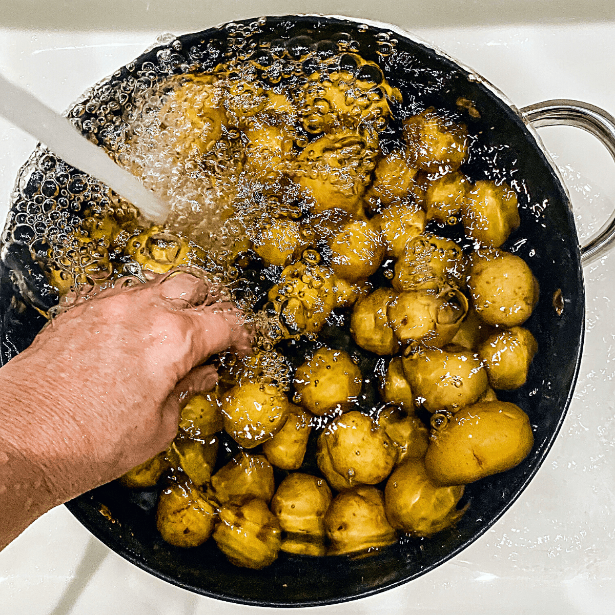 Potatoes are in a large pot with water filling the pot and cooling the potatoes.