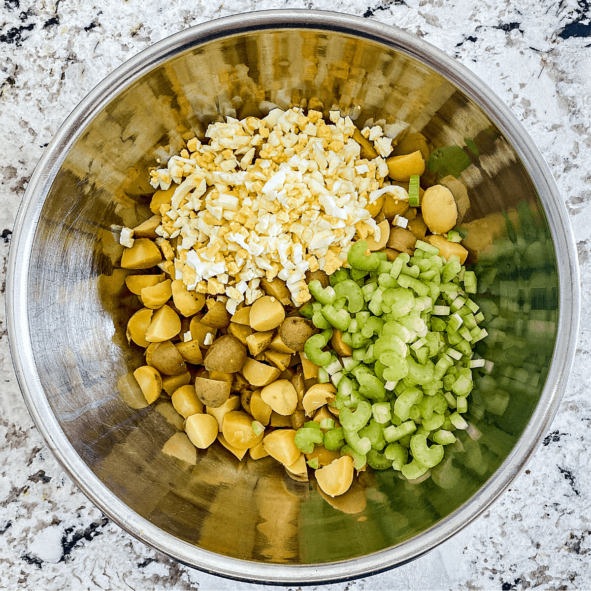In a large steel mixing bowl: quartered cooked gold potatoes, chopped eggs, and chopped celery.