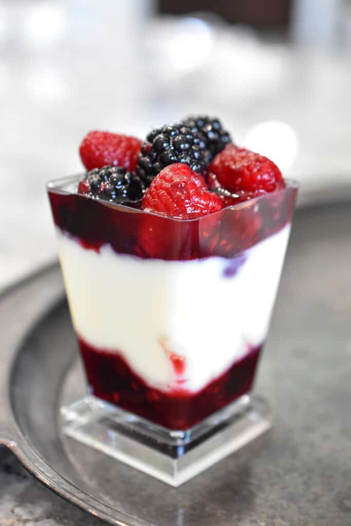 A petite parfait of white cheesecake pudding with layers of red raspberries and blackberries in a red wine dessert sauce.