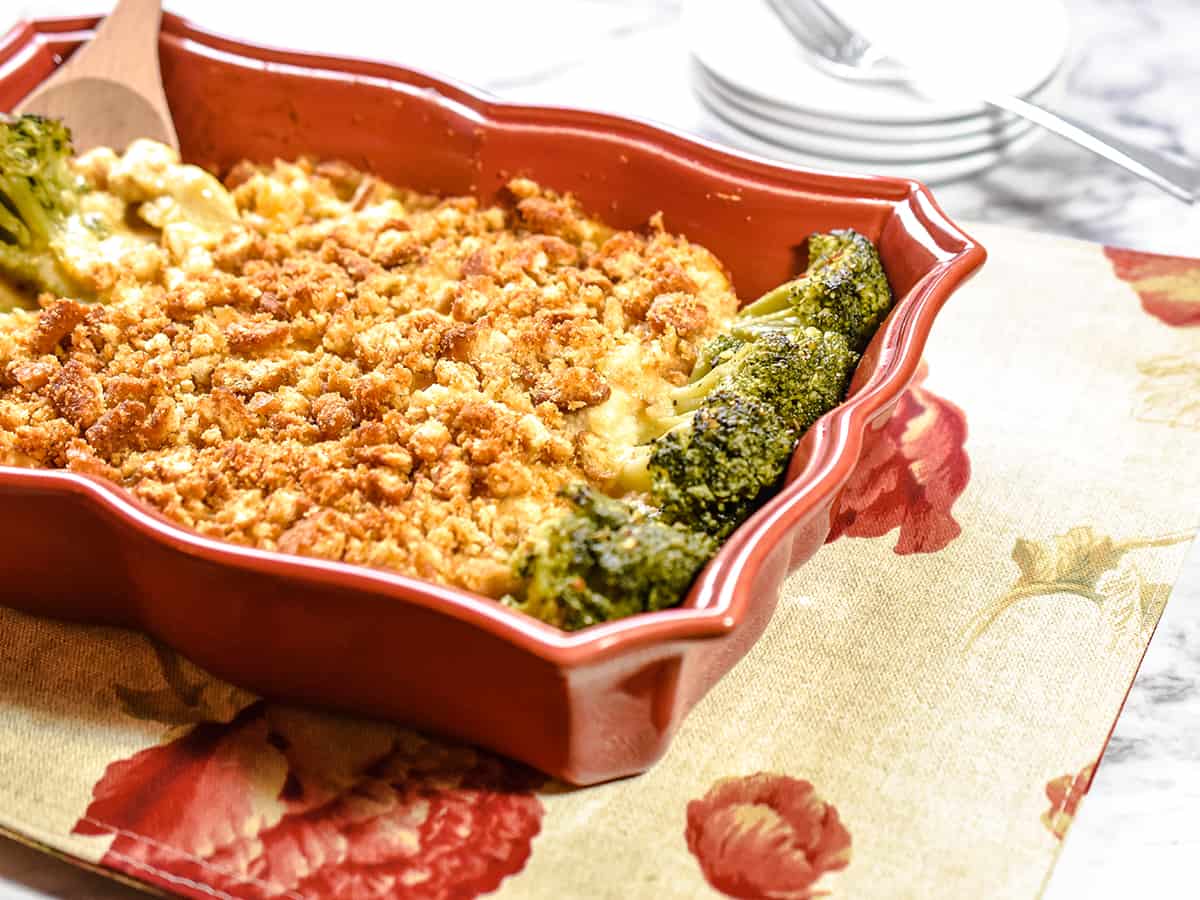 A red casserole containing leftover turkey and broccoli in an Alfredo and extra cheese sauce. Plates and a fork are in the background.