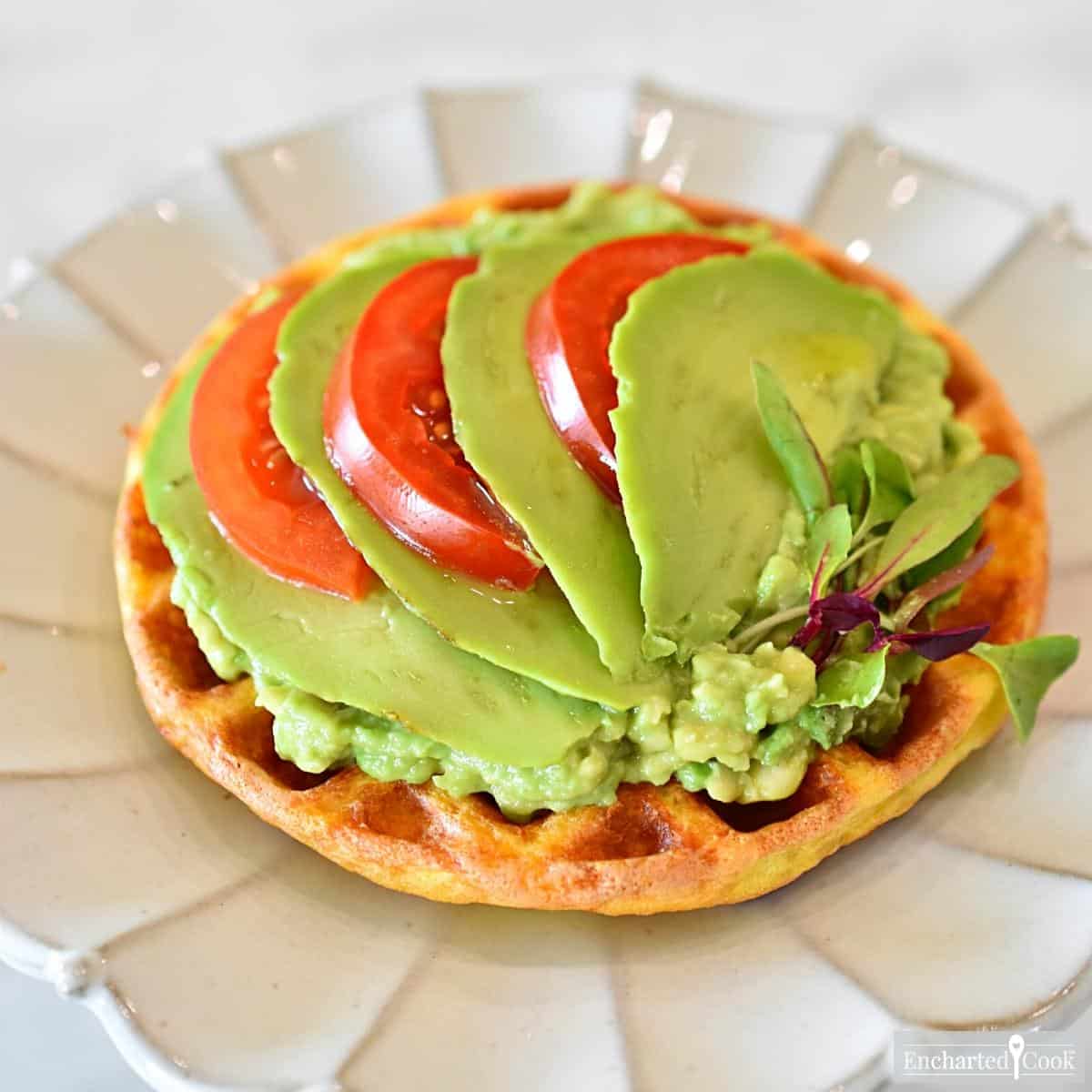 Mashed and sliced avocado with slices of tomato on a cheese waffle.