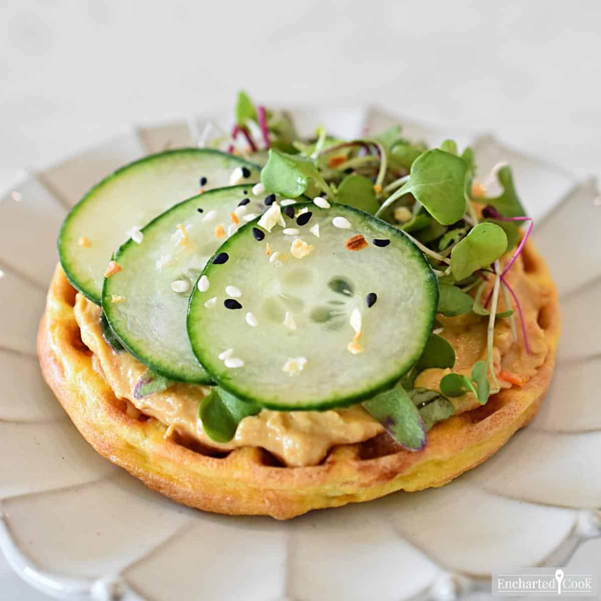 Red pepper hummus and sliced cucumber on a cheese waffle.