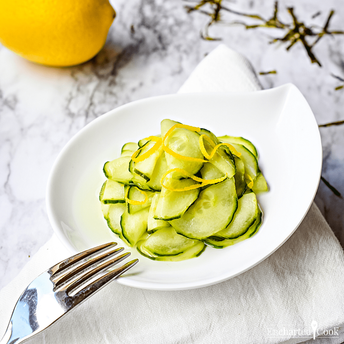 A white dish of pickles garnished with lemon zest.