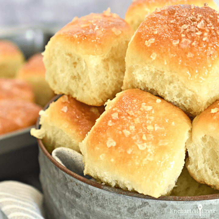 Close-up view of dinner rolls piled into a rustic tin serving stand.