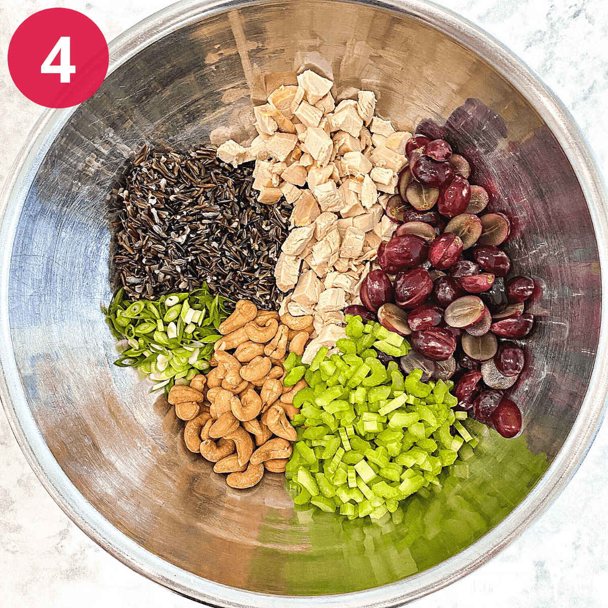 The salad ingredients in a large bowl: wild rice, cubed cooked chicken, halved red grapes, chopped celery, whole cashews, and slice green onions.