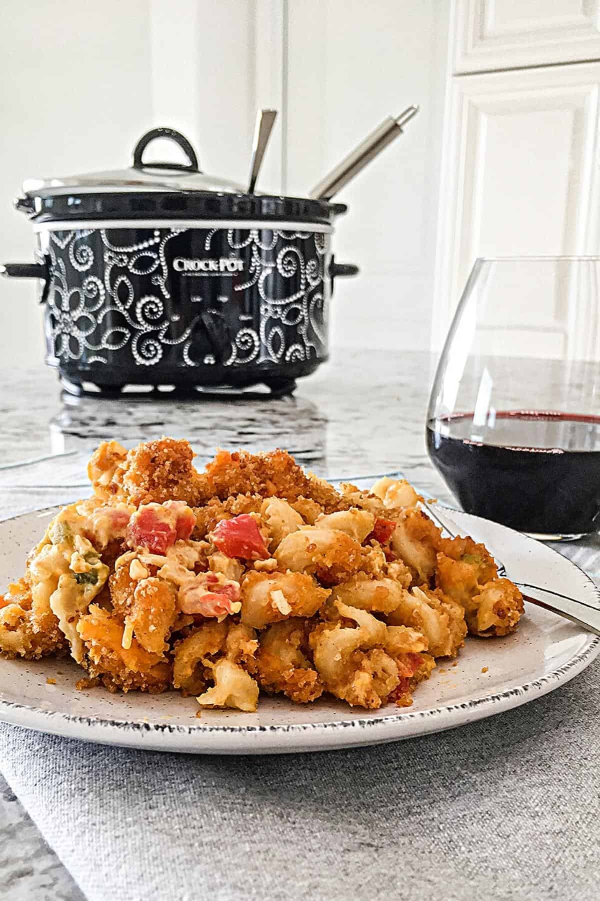A plate loaded with mac and cheese with a slow cooker in the background.