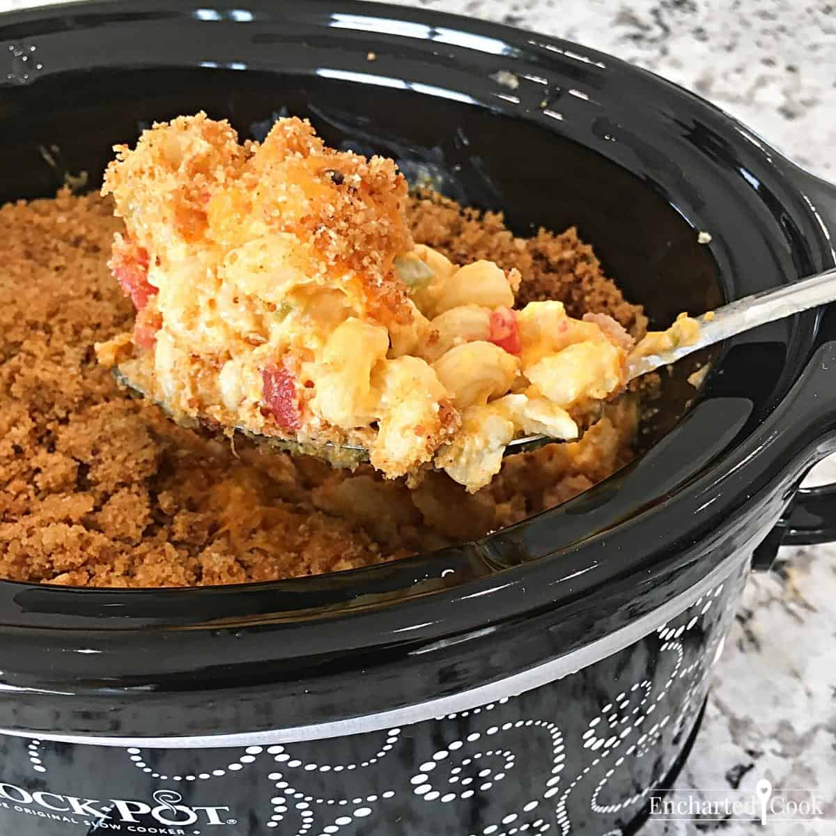 Scooping out a portion of mac and cheese from the slow cooker with a large spoon.