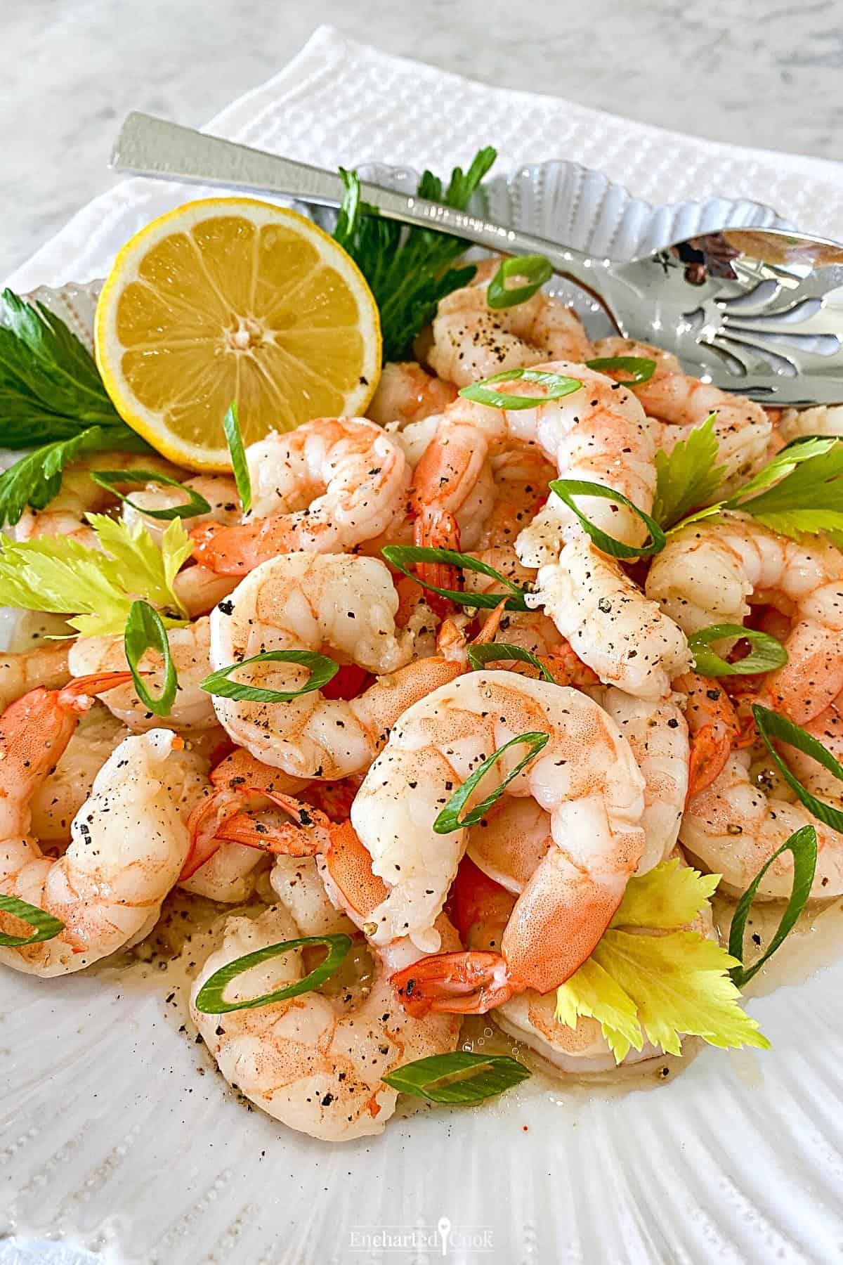 Vertical image of a plate of shrimp garnished with green onions, celery leaves, and a lemon half.
