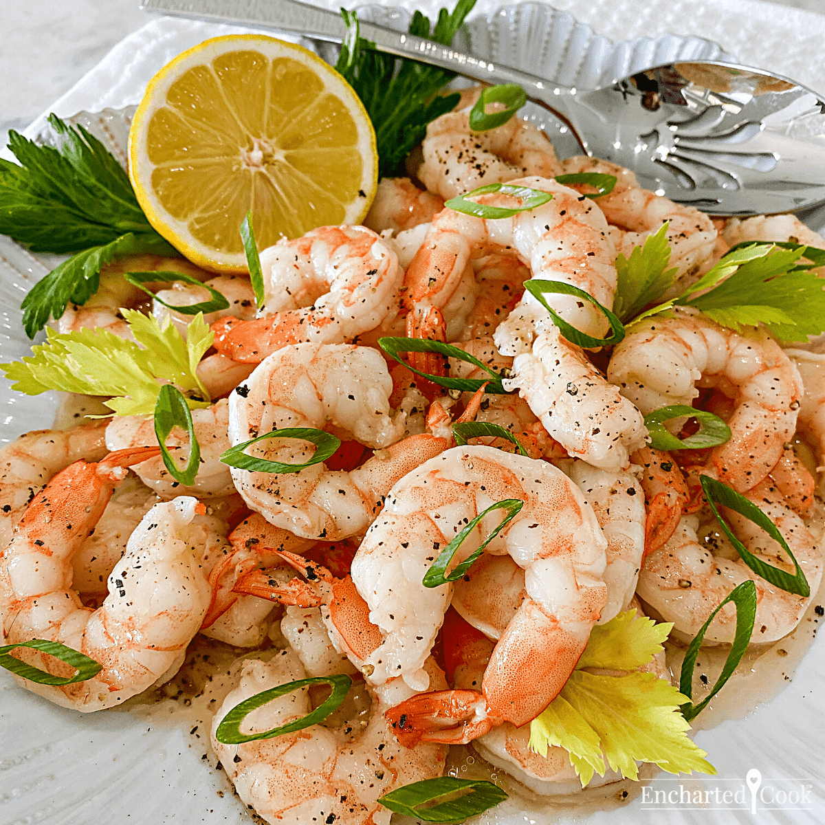 Square image of a plate of shrimp garnished with green onions, celery leaves, and a lemon half.