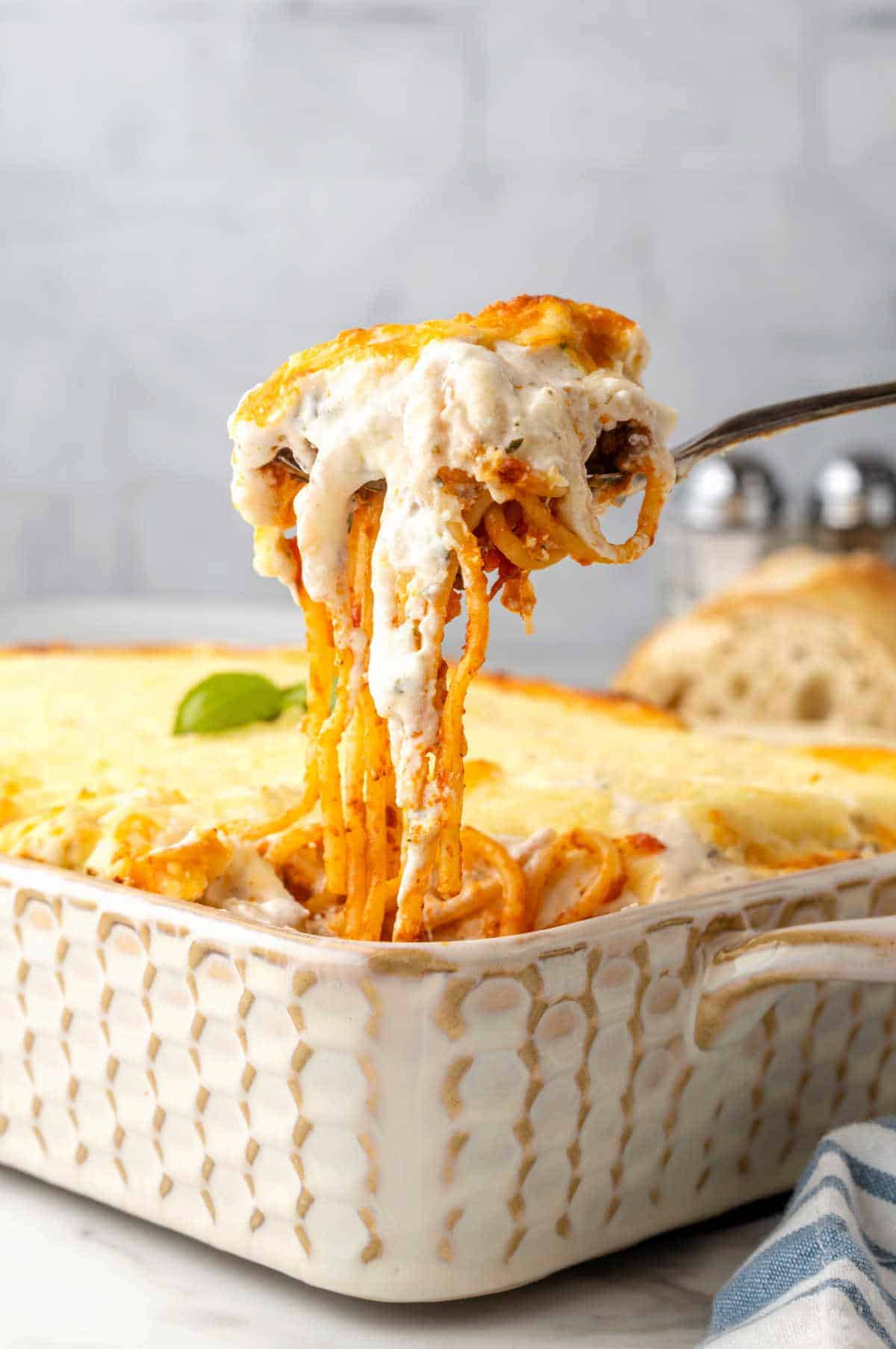A fork full with spaghetti, sauce, and cheese over a beige casserole.