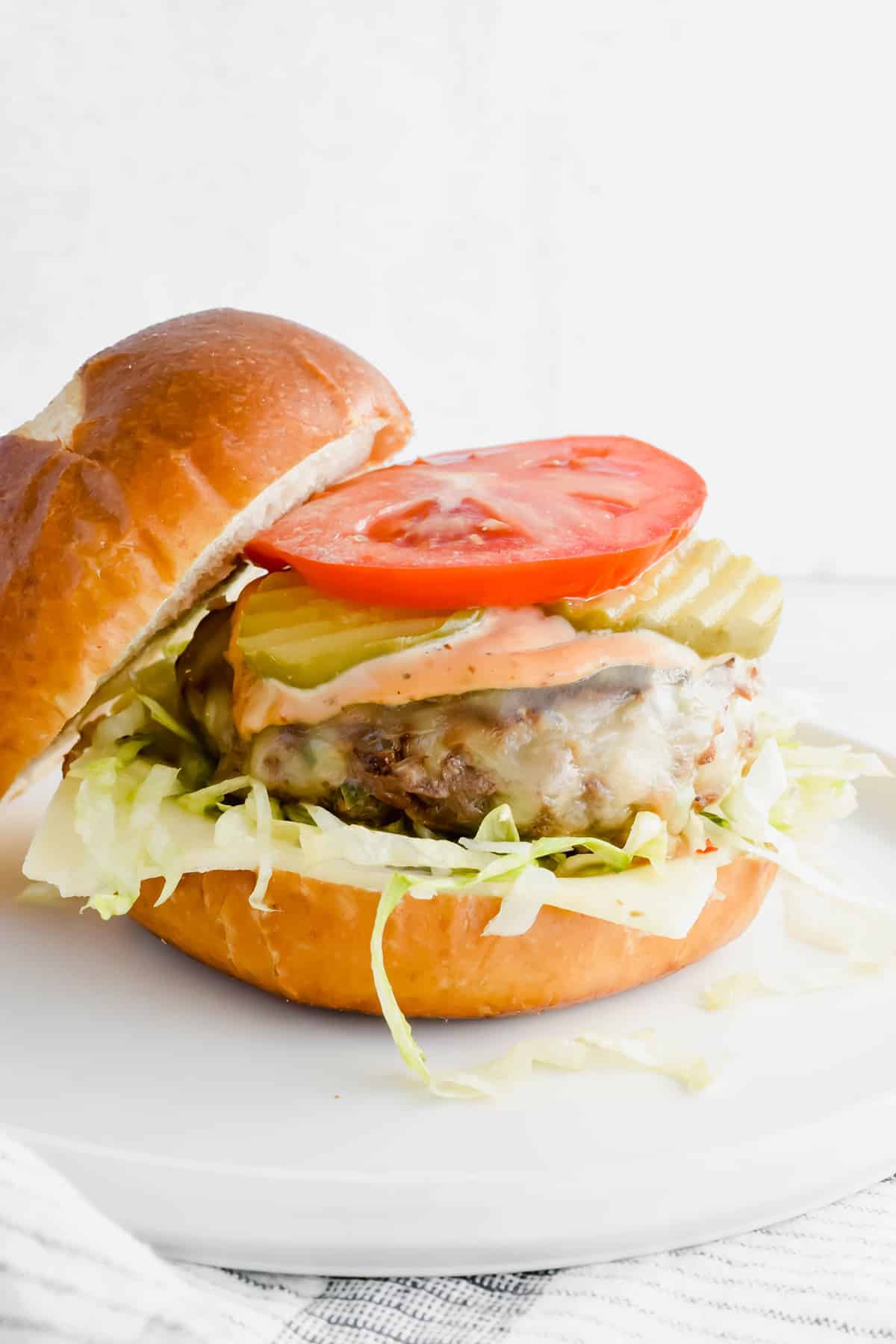 Ground beef burgers with onions and cheese with lettuce, tomato, and pickles.