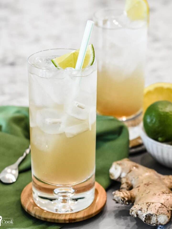 A golden brown beverage in a tall glass with a lime wedge and a straw.
