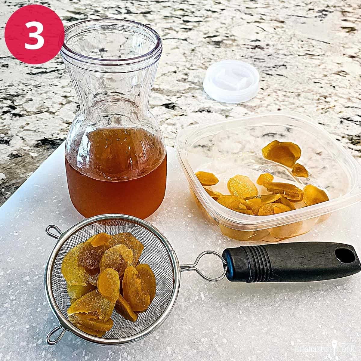 Strained ginger syrup in a carafe, slices of cooked ginger in a container, and a strainer with slices of cooked ginger.