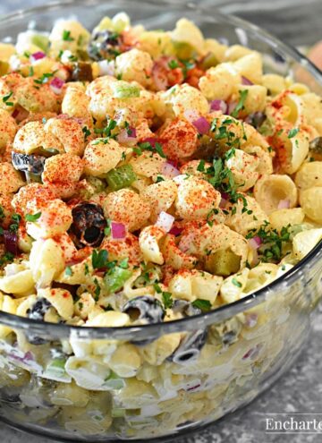 Macaroni salad with red onion and black olives in a glass bowl.