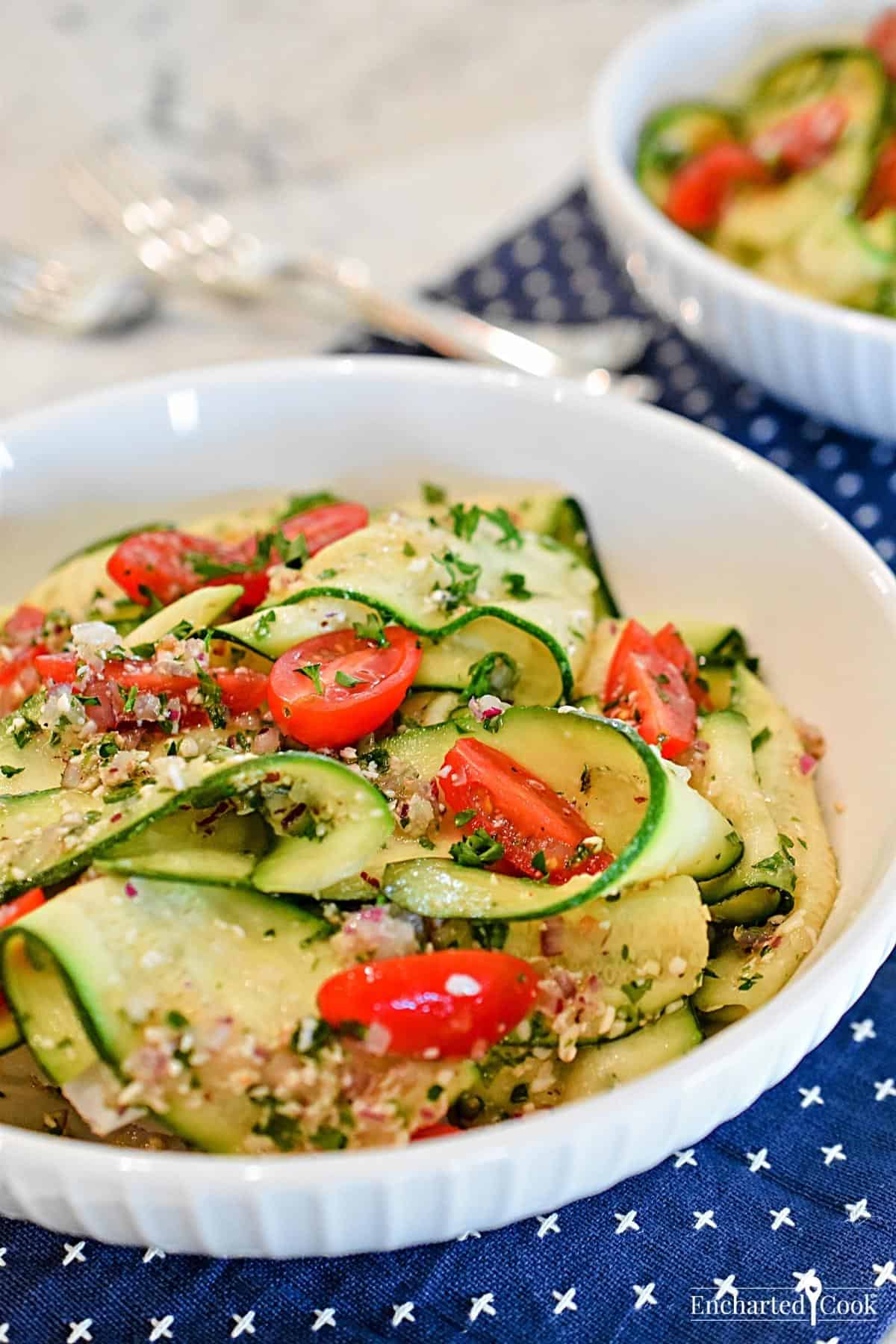 A white bowl filled with ribbons of zucchini and cherry tomatoes.